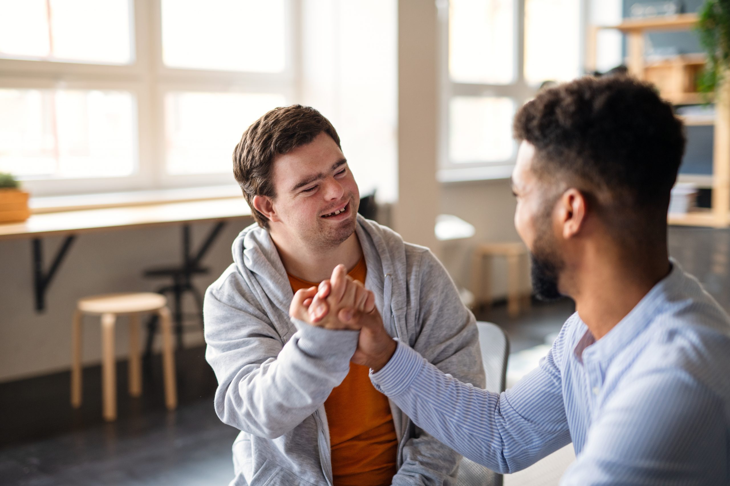 A young happy man with Down syndrome with his mentoring friend celebrating success indoors at school